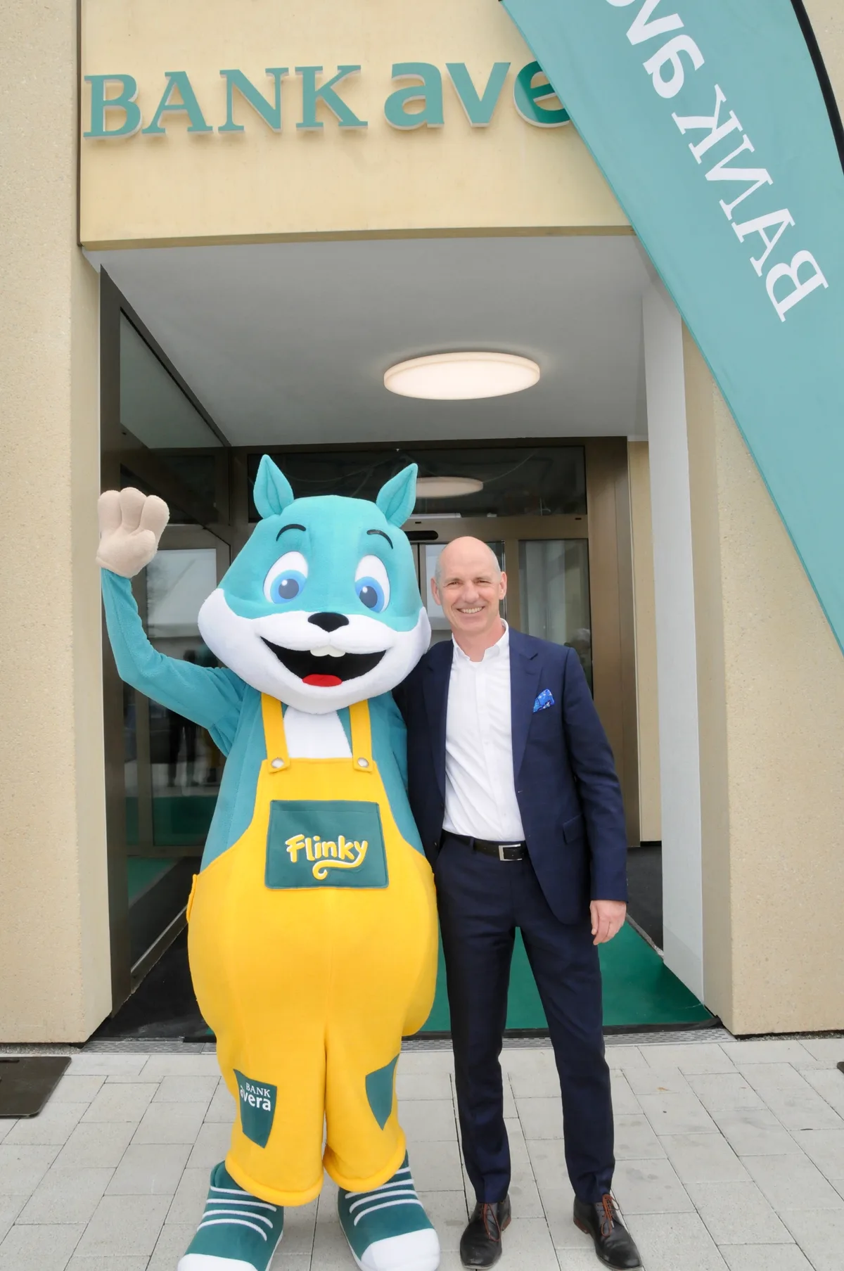Man sieht den Filialleiter der Bank Avera mit dem Maskottchen Flinky.